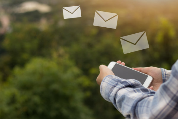 Person holding mobile phone with email icons floating away from it