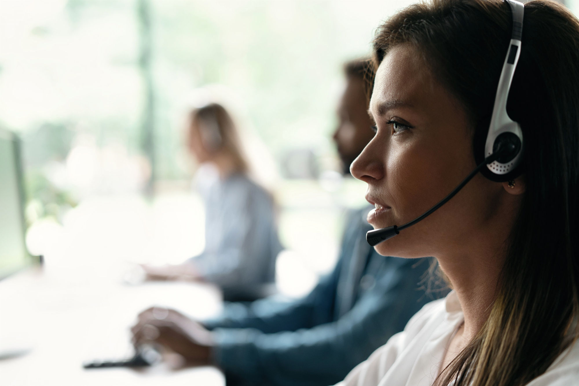Friendly smiling woman call center operator with headset using computer at office