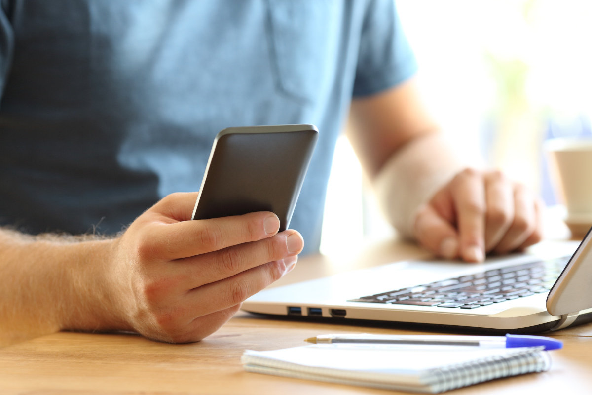 Man sitting at desk using laptop and mobile phone